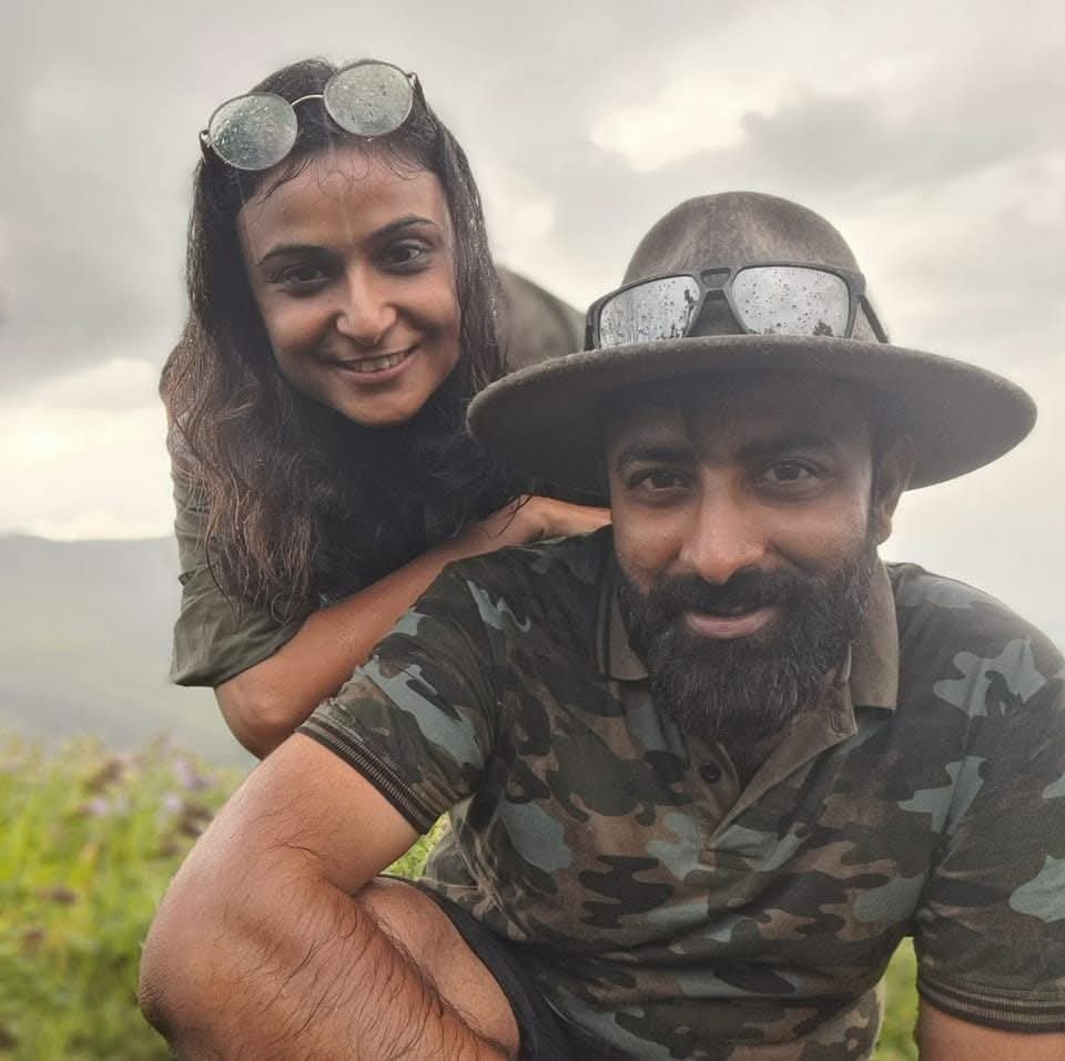 Honey Dhawan and her husband Amith Bangre smiling together on a misty, grassy hillside during their travels